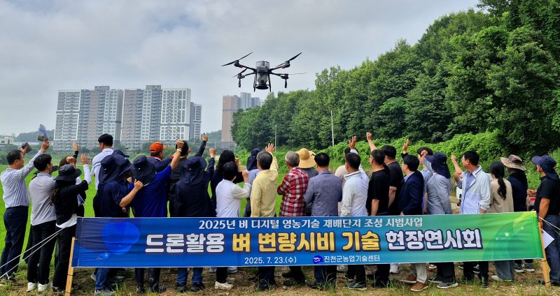 [진천=뉴시스] 23일 충북 진천군 덕산읍 신척리 시범단지에서 열린 '드론 활용 벼 변량 시비 기술 현장 연시회' 참석자들이 드론을 향해 손을 들어 흔들고 있다. (사진=진천군농업기술센터 제공) 2025.07.23. photo@newsis.com