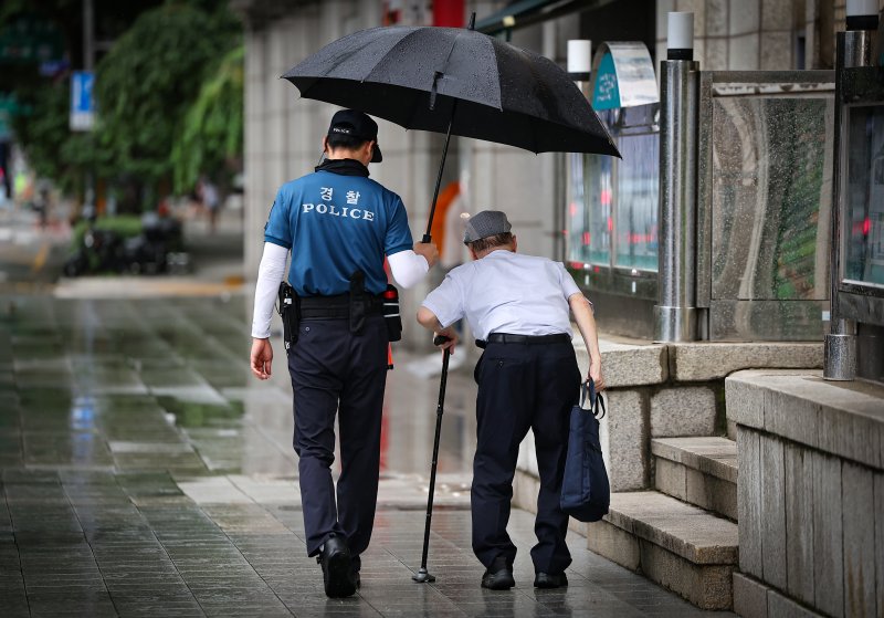 오전 비가 내리는 서울 종로구 광화문역 인근에서 경찰관이 한 어르신에게 우산을 씌어주고 있다. 2024.8.7/뉴스1 ⓒ News1 김진환 기자