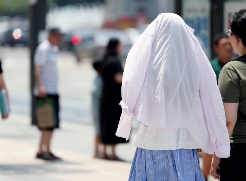 [서울=뉴시스] 김진아 기자 = 폭염이 연일 이어지고 있는 25일 서울 종로구 광화문광장 인근에서 한 시민이 옷으로 햇볕을 가리고 걸어가고 있다. 2025.07.25.bluesoda@newsis.com