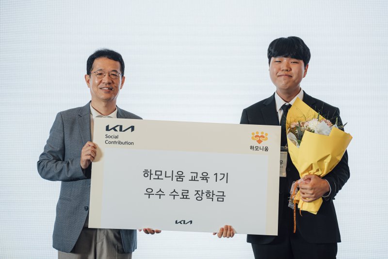 기아 지속가능경영실장 이덕현 상무(왼쪽)가 지난 7일 '하모니움 교육 프로그램' 1기 수료생 오민우 학생에게 우수 수료생 시상을 한 뒤 기념촬영을 하고 있다. 기아 제공