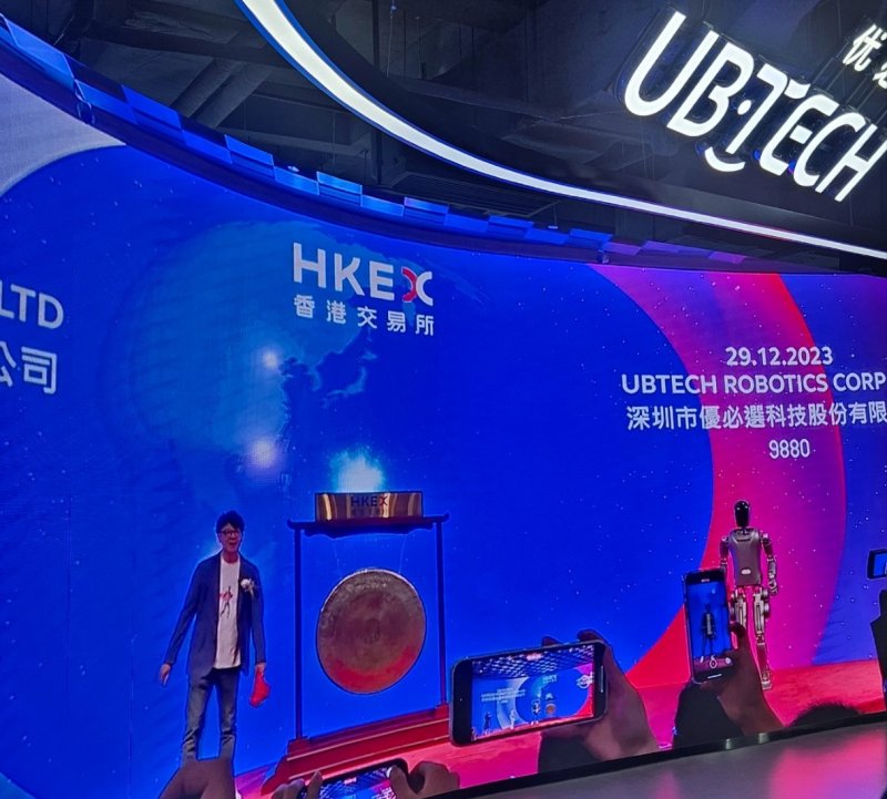 유비테크 창업자 저우젠이 2023년 말 홍콩증권거래소 상장 행사에 자사 휴머노이드 로봇과 함께 징을 치기 위해 준비하고 있는 모습.