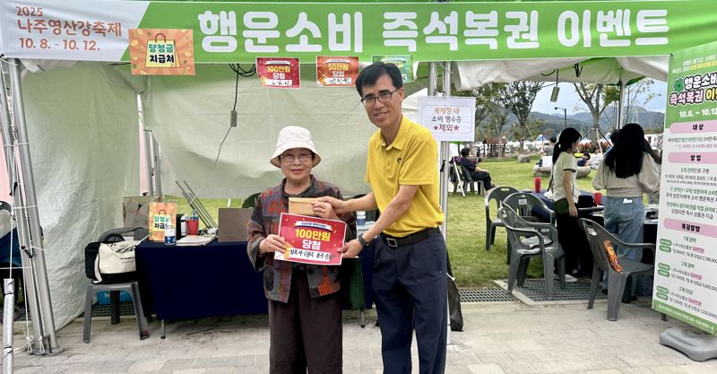 전남 나주시는 지난 8일부터 오는 12일까지 일정으로 진행 중인 '2025 나주영산강축제'의 '행운소비 즉석복권 이벤트'가 시민과 관광객의 큰 호응을 얻으며 지역 경제 활성화에 활력을 불어넣고 있다고 밝혔다. 사진은 지난 9일 '행운소비 즉석복권 이벤트' 첫 100만원 당첨 주인공인 김옥자 씨(왼쪽)가 축제 관계자와 기념사진을 촬영하고 있는 모습. 나주시 제공