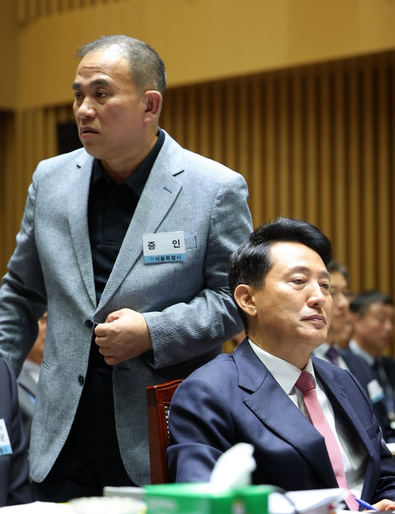 [서울=뉴시스] 김선웅 기자 = '정치브로커'로 알려진 명태균 씨가 23일 서울시청에서 열린 국회 행정안전위원회의 서울특별시에 대한 국정감사에 증인으로 출석해 오세훈 서울시장 뒤를 지나 증언대로 향하고 있다. 2025.10.23. mangusta@newsis.com