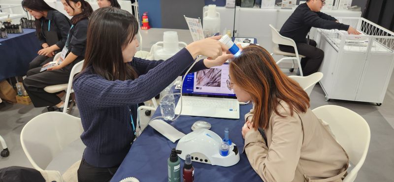 K-뷰티공동관을 찾은 여성 관람객이 두피·피부진단 체험을 하면서 관계자로부터 두피 상태 등에 대해 설명을 듣고 있다. 김장욱 기자