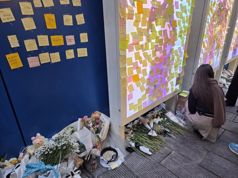 [서울=뉴시스]김윤영 수습기자=31일 서울 용산구 이태원역 1번 출구 인근 '10·29 기억과 안전의 길'에 마련된 추모공간. 시민이 희생자들을 기리며 메시지가 적힌 포스트잇을 바라보고 있다. 바닥에는 국화꽃과 편지, 음료수 등이 놓여 있다. 2025.10.31