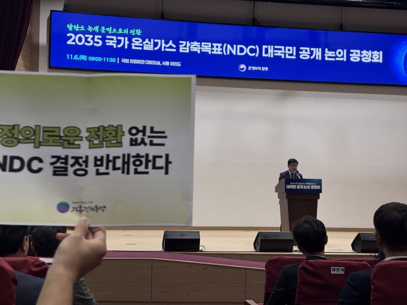 6일 서울 영등포구 국회의원회관 대회의실에서 열린 2035 국가온실가스 감축목표 대국민 공개 논의 공청회에서 김성환 장관이 발언 중인 가운데 환경단체 회원들이 손피켓을 들어보이고 있다. 기후에너지환경부는 2035년 국가온실가스감축목표(NDC)를 2018년 대비 50~60% 감축 범위에서 확정할 예정이다. 2025.11.6/뉴스1 ⓒ News1 황덕현 기후환경전문기자