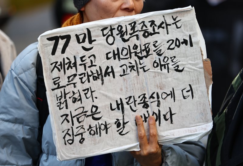 [서울=뉴시스] 김명년 기자 = 1일 오후 서울 여의도 더불어민주당사 앞에서 한 민주당원이 정청래 대표의 '대의원·권리당원 1인1표제' 대한 규탄 피켓을 들고 있다. 2025.12.01. kmn@newsis.com