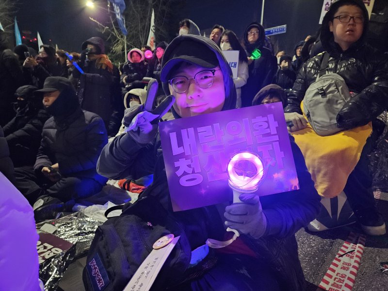 3일 여의도 국회 앞에서 열린 시민대행진에 참석한 30대 전재현 씨가 응원봉과 피켓을 들고 V자 포즈를 취하고 있다. 2025.12.03/ⓒ 뉴스1 유채연 기자