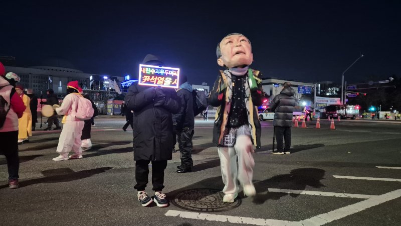[서울=뉴시스] 전상우 수습기자 = 3일 오후 서울 여의도 국회의사당 인근에서 열린 '내란청산·사회대개혁 시민대행진'에서 한 참가자가 윤석열 전 대통령을 풍자한 대형 탈을 쓰고 춤을 추고 있다. 옆 참가자는 '내란수괴 윤석열을 심판하라'는 LED 피켓을 들고 있다. 2025.12.03. swoo@newsis.com