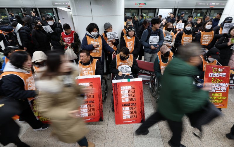 [서울=뉴시스] 이영환 기자 = 전국장애인차별철폐연대(전장연) 회원들이 4일 오전 서울 종로구 지하철5호선 광화문역에서 열린 '제67차 출근길 지하철 탑니다’ 시위를 하는 가운데 시민들이 이동하고 있다. 2025.12.04. 20hwan@newsis.com
