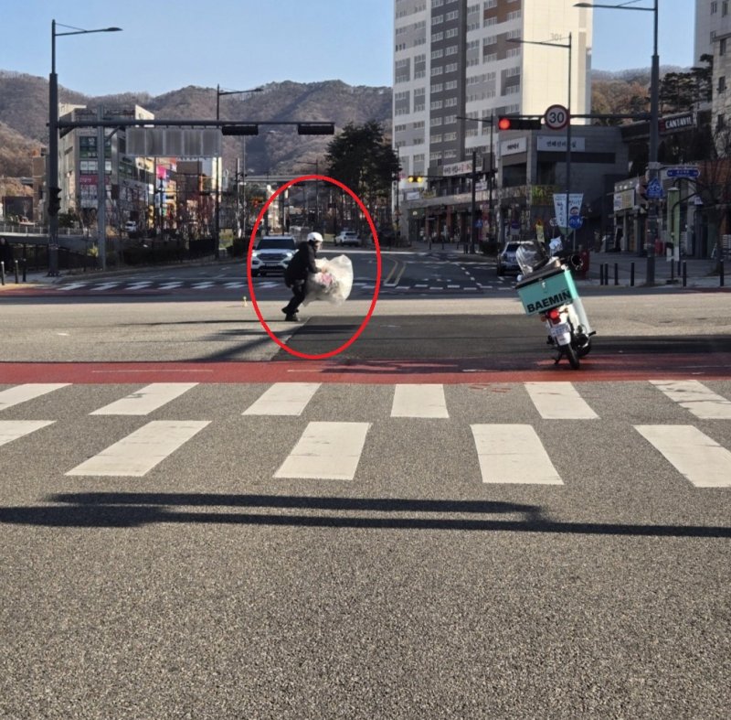 [서울=뉴시스] 교차로 한복판에 큰 쓰레기 봉투가 놓여있는 것을 발견한 배달기사가 뛰어가 이를 치우고 있다. (사진출처: 보배드림 캡처) 2025.12.04.