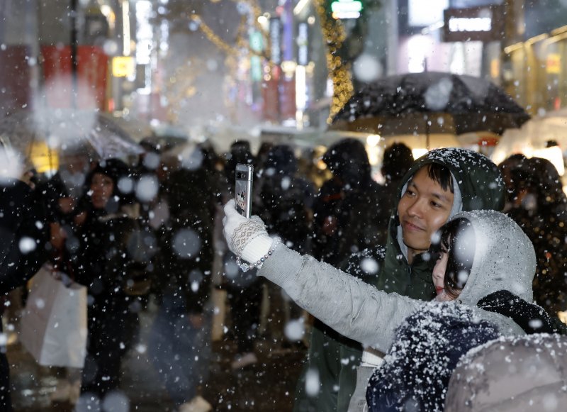 첫눈이 내린 4일 오후 서울 중구 명동을 찾은 관광객들이 내리는 눈을 맞으며 즐거운 시간을 보내고 있다. 기상청은 "퇴근 시간대 강한 눈이 내릴 가능성이 크다＂며 동네 예보와 실시간 날씨를 확인할 것을 당부했다. 2025.12.4/뉴스1 ⓒ News1 박정호 기자