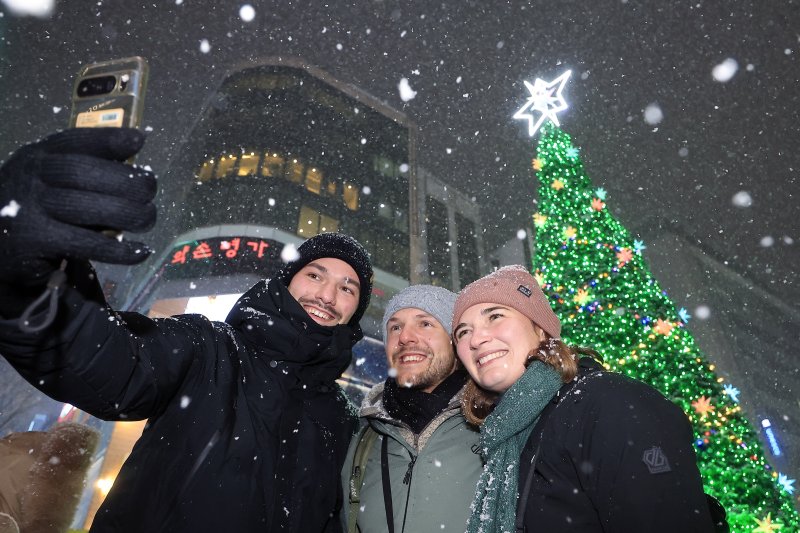 첫눈이 내린 4일 오후 서울 중구 명동을 찾은 관광객들이 내리는 눈을 맞으며 즐거워하고 있다. 기상청은 "퇴근 시간대 강한 눈이 내릴 가능성이 크다＂며 동네 예보와 실시간 날씨를 확인할 것을 당부했다. 2025.12.4/뉴스1 ⓒ News1 박정호 기자