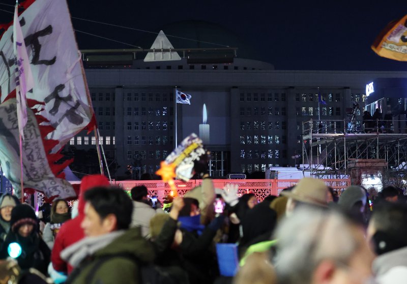 12·3 비상계엄 1년을 맞아 서울 국회의사당 외벽에 계엄 해제 당시를 되새기는 ‘미디어 파사드’가 펼쳐지고 있다. 화면에는 촛불 하나가 켜진 장면이 연출되고 있고 국회 밖에서는 시민들이 행진을 이어가고 있다. 2025.12.3/뉴스1 ⓒ News1 박지혜 기자