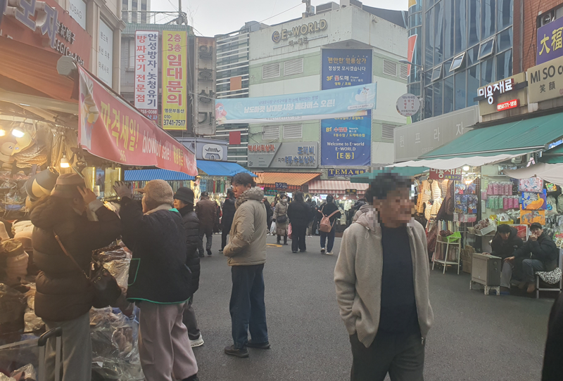 지난 6일 오후 서울 중구 남대문시장에서 손님들이 모자를 시착하고 있다. 한켠에는 시장 상인들이 난로 앞에서 몸을 녹이는 모습. 사진=최승한 기자