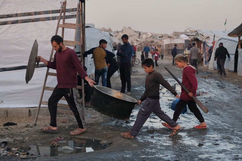 [자발리아=AP/뉴시스] 지난 7일(현지 시간) 가자지구 북부 자발리아 난민촌에서 한 남성과 아이들이 조리 기구를 들고 진흙탕이 된 통로를 지나고 있다. 2025.12.09.