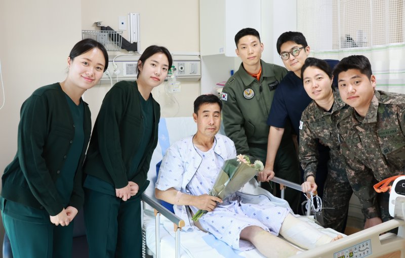 육군은 지난 1일 육군 3군단 직할 항공단 소속 이지홍 대위가 공사 중 차량사고로 생명이 위급한 민간인을 응급조치하고 신속한 판단으로 군 의무후송헬기(메디온)으로 이송해 소중한 생명을 구했다고 10일 밝혔다. 박병춘 씨가 병문안을 온 이지홍 대위(오른쪽 네번째), 국군외상센터 의료팀들과 함께 기념 촬영하고 있다. 육군 제공