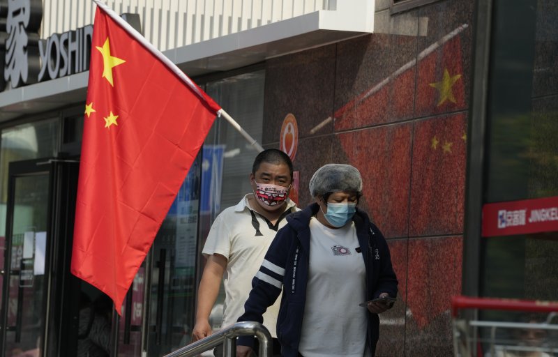 [베이징=AP/뉴시스]지난 10월7일 중국 수도 베이징에서 중국 국경절 연휴 마지막 날 마스크를 쓴 주민들이 중국 국기 옆을 지나가고 있는 모습. 2022.12.29.