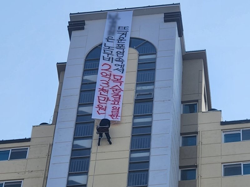[나주=뉴시스] 10일 오후 1시께 전남 나주시 빛가람동 한 20층 높이 아파트에서 해당 아파트 도장 업체 관계자 A(52)씨가 현수막을 내걸어 체불임금 지급을 촉구하며 고공농성을 벌이고 있다. (사진 = 독자 제공) 2025.12.10. photo@newsis.com