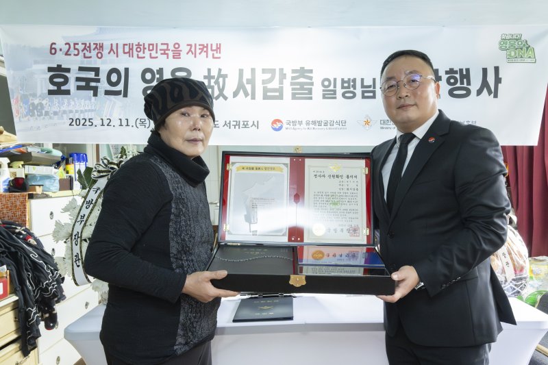 [서울=뉴시스] 고 서갑출 일병의 며느리인 이정순 씨(72)와 조해학 국방부유해발굴감식단장 직무대리(육군 중령)가 함께 전사자 신원확인 통지서를 들고 기념사진을 촬영하고 있다. (사진=국방부 제공) 2025.12.11. photo@newsis.com *재판매 및 DB 금지