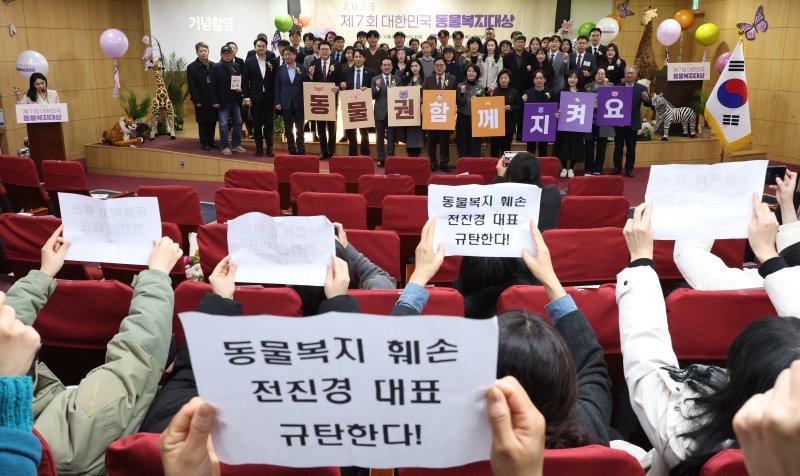 [서울=뉴시스] 김금보 기자 = 동물권행동 카라 활동가들과 후원회원들이 9일 서울 여의도 국회 의원회관에서 열린 2025 제7회 대한민국 동물복지대상 시상식에서 기념촬영을 하는 참석자들을 향해 전진경 동물권행동 카라 대표를 규탄하는 손팻말을 들고 있다. 2025.12.09. kgb@newsis.com