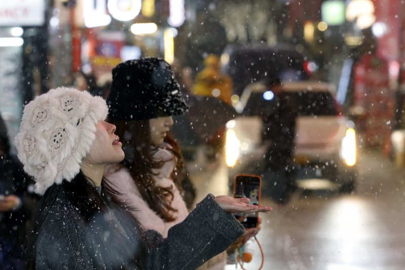 첫눈이 내린 4일 오후 서울 중구 명동을 찾은 관광객들이 내리는 눈을 맞으며 즐거워하고 있다. 기상청은 "퇴근 시간대 강한 눈이 내릴 가능성이 크다＂며 동네 예보와 실시간 날씨를 확인할 것을 당부했다. 2025.12.4/뉴스1 ⓒ News1 박정호 기자