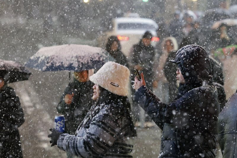 첫눈이 내린 4일 오후 서울 중구 명동을 찾은 관광객들이 내리는 눈을 맞으며 즐거운 시간을 보내고 있다. 기상청은 "퇴근 시간대 강한 눈이 내릴 가능성이 크다＂며 동네 예보와 실시간 날씨를 확인할 것을 당부했다. 2025.12.4/뉴스1 ⓒ News1 박정호 기자