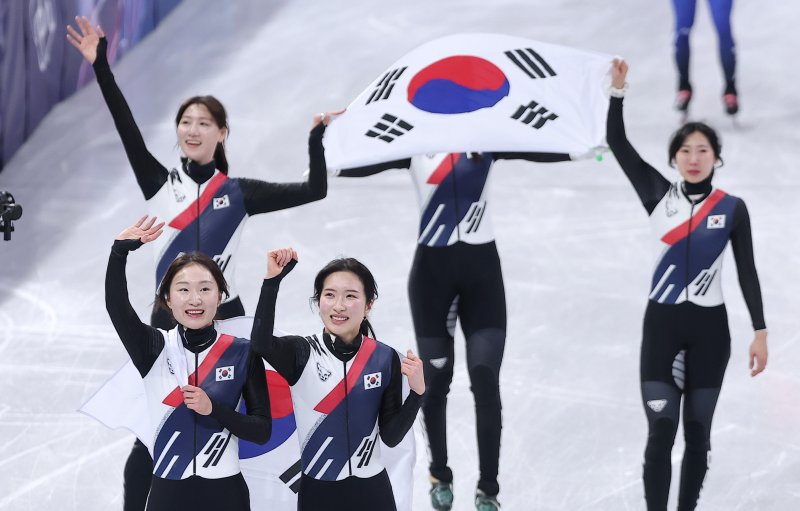 대한민국 여자 쇼트트랙 대표팀이 19일 이탈리아 밀라노 아이스스케이팅 아레나에서 열린 2026 밀라노·코르티나담페초 동계올림픽 쇼트트랙 여자 3000m 계주 결승에서 금메달을 차지한 후 태극기를 두르고 관중석을 향해 인사하고 있다. 뉴스1