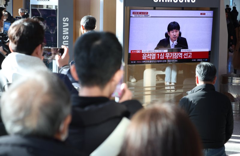 [서울=뉴시스] 이영환 기자 = 19일 오후 서울 용산구 서울역에서 시민들이 '내란 우두머리 혐의' 윤석열 전 대통령의 1심 선고 공판 중계를 시청하고 있다. 윤 전 대통령은 1심에서 무기징역을 선고 받았다. 2026.02.19. 20hwan@newsis.com