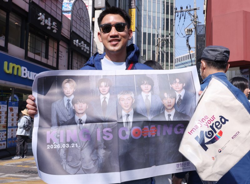 방탄소년단(BTS) 컴백 공연일인 21일 오전 서울 광화문광장 인근에서 외국인 관광객이 BTS 관련 특별판을 들고 기념촬영을 하고 있다. 2026.3.21 ⓒ 뉴스1 박지혜 기자