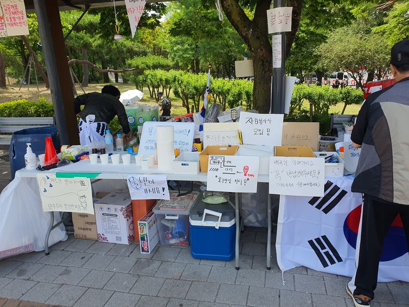 시민들이 집회 현장에 마련된 자원봉사 부스에서 물과 컵 등 물품을 정리하고 있다. 사진=최승한 기자