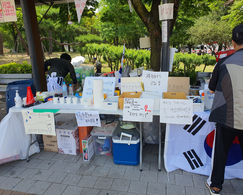 시위 현장 한쪽에 물과 컵, 태극기, 손팻말 등이 비치된 자원봉사 공간이 마련돼 있다. 사진=최승한 기자