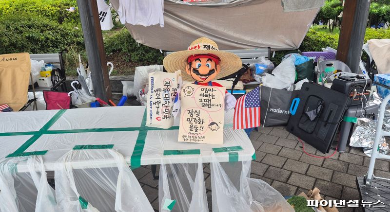 올림픽공원 재선거 요구 집회 천막에 슈퍼마리오 가면과 손글씨 피켓, 태극기와 성조기가 놓여 있다. 사진=한승곤 기자
