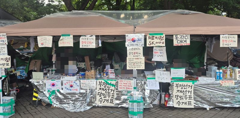 재선거 요구 집회 천막에서 자원봉사자들이 물품을 정리하고 있다. 천막 앞에는 재선거·당일투표·수개표를 요구하는 피켓이 붙어 있다. 사진=한승곤 기자