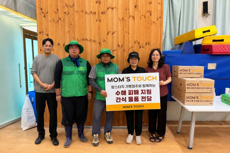 지난 25일 경남 거제시 거제 장평초등학교 집중호우 피해현장에서 유성재 맘스터치 상생협력그룹장(왼쪽)이 거제시 주민과 자원봉사자들에게 간식 물품을 전달한 뒤 기념 촬영을 하고 있다. 맘스터치앤컴퍼니 제공