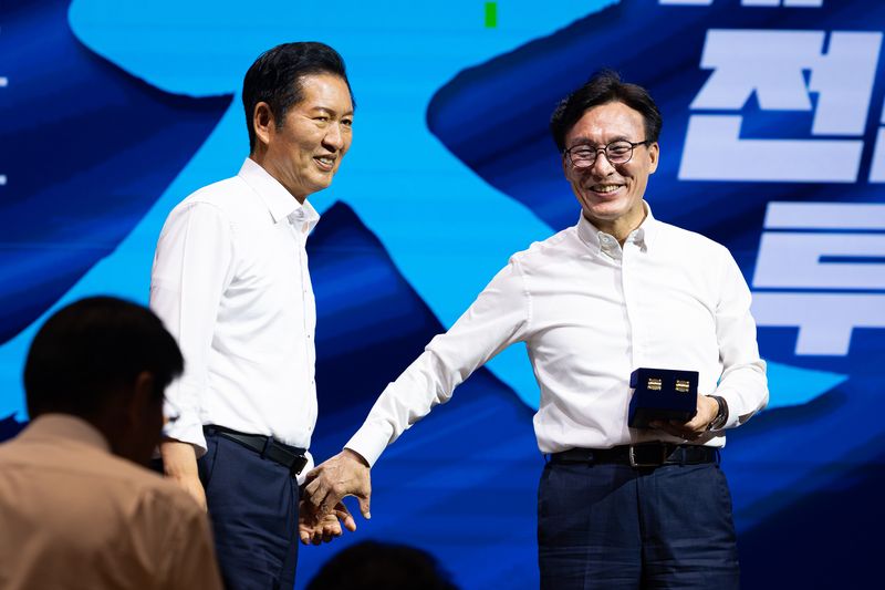김민석 더불어민주당 대표가 27일 인천 영종구 인스파이어 엔터테인먼트 리조트에서 열린 2026년 정기국회 대비 국회의원 워크숍에서 정청래 전 대표에게 감사패 전달에 앞서 손을 잡고 있다. 뉴스1