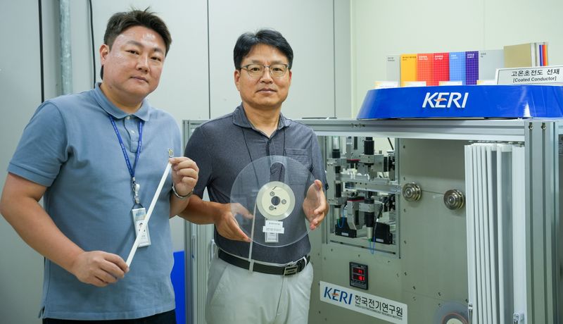 한국전기연구원(KERI) 박인성·하홍수 박사(왼쪽부터)가 고온초전도 선재를 들고 3D 비접촉 초정밀 검사 장비 옆에서 포즈를 취하고 있다. 한국전기연구원 제공