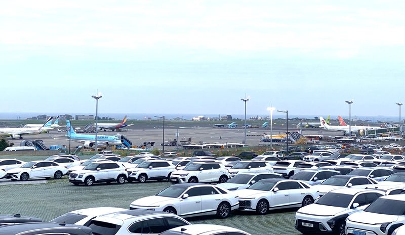 제주국제공항 인근 렌터카 업체 차고지에 차량들이 줄지어 주차돼 있고 뒤편 공항 계류장에는 여객기들이 서 있다. 사진=파이낸셜뉴스