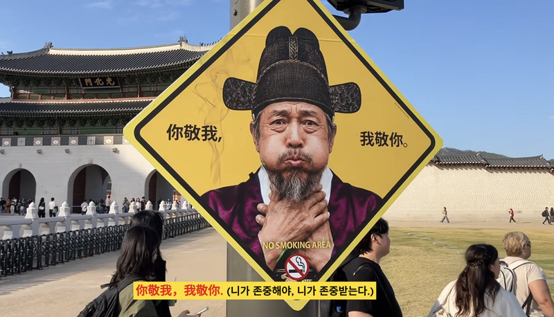 조선시대 문관이 담배 연기에 목을 움켜쥔 모습을 담은 금연 표지판이 26일 서울 광화문 앞에 설치돼 있다. 표지판에는 '你敬我, 我敬你(당신이 나를 존중하면 나도 당신을 존중한다)'라는 중국어 문구가 적혀 있다. /사진=유튜브 '이제석의 광고 아카이브' 캡처